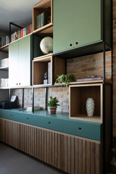 Home office com estante de nichos em verde e madeira sobre parede de tijolinho